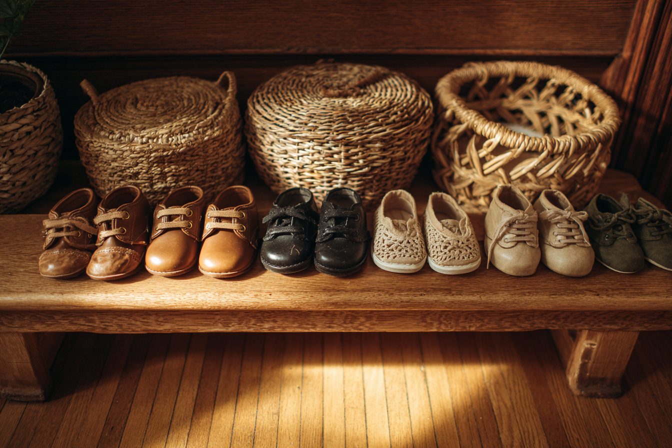 Six pairs of toddler shoes lined up on a wooden bench